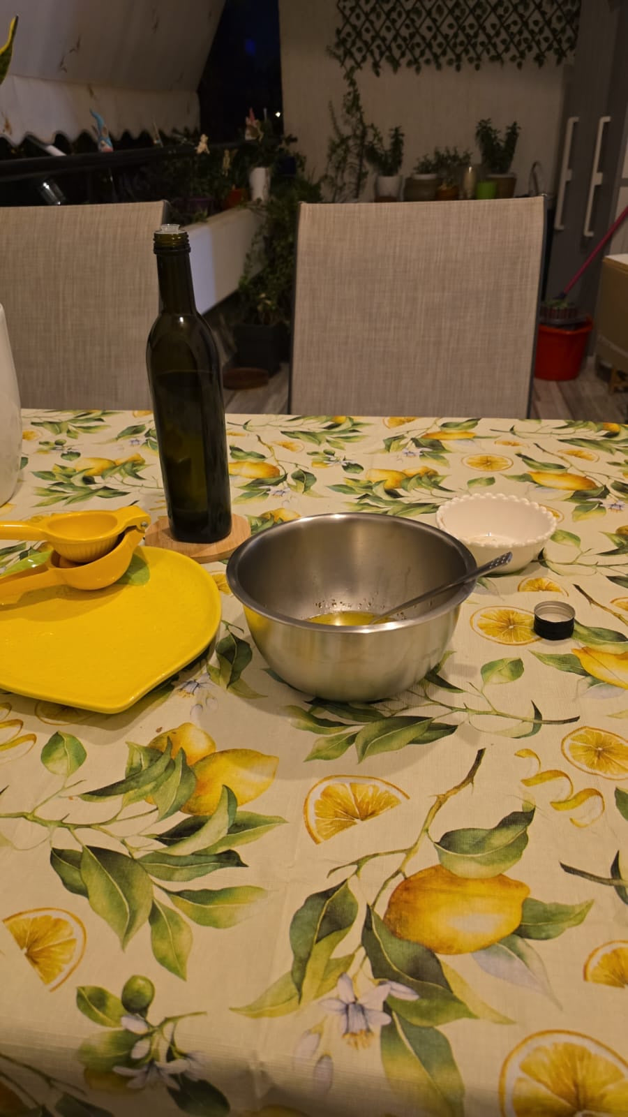 Ladolemono being whisked in a steel bowl, with a lemon squeezer and a bottle of olive oil on a lemon-print tablecloth